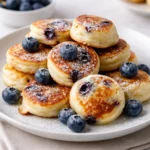 Golden Blueberry Lemon Pancake Bites on a white plate with powdered sugar.