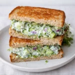 Two Easy Cucumber Salad Sandwiches on a white plate with fresh sprouts.