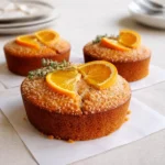 A glazed orange ginger honey cake topped with zest on a wooden table.